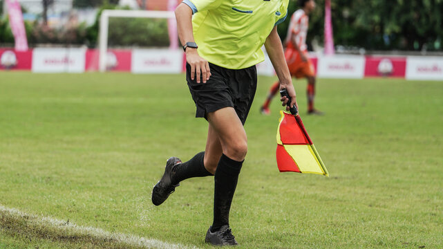 Assistant referee running with signal flag during outdoor soccer match on wet grass field