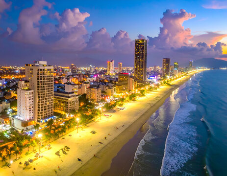 Stunning Coastal Cityscape at Dusk with Illuminated Buildings and Ocean Waves.