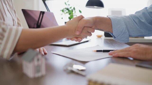 Real estate agent and client shaking hands after signing a contract for a new house purchase, sealing a successful deal with a handshake and receiving the keys