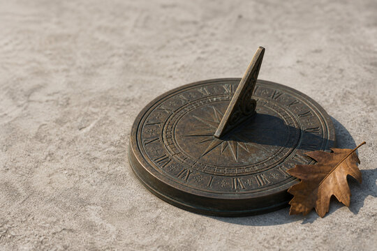 Antique bronze sundial with dried oak leaf on grey stone, time and history concept