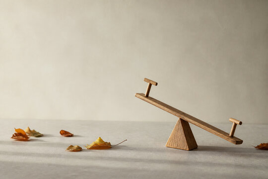 Tiny tilted wooden seesaw model with scattered autumn leaves, balance and prepared practical concept.