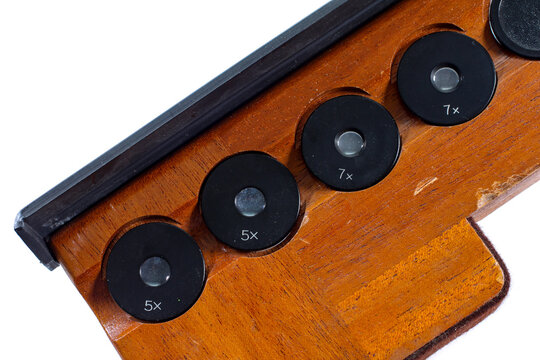 Vintage microscope optical accessories with 5x and 7x magnification lenses arranged in a wooden case, isolated against a white background.