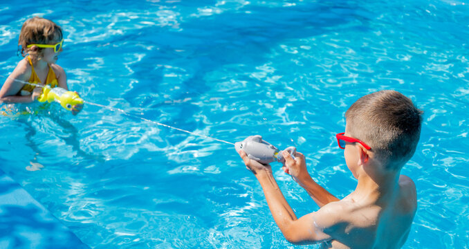 Children shooting water guns in swimming pool, water jet splash