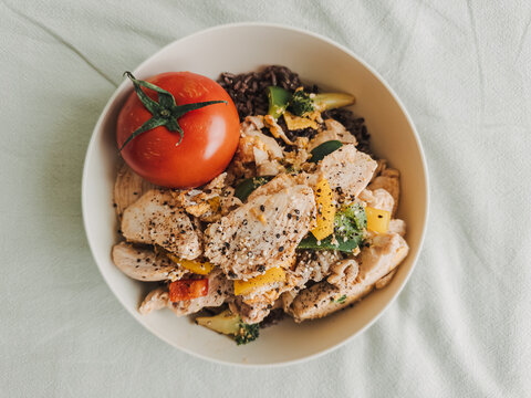 Nutritious chicken breast meal with colorful vegetables, black rice, and a fresh red tomato.