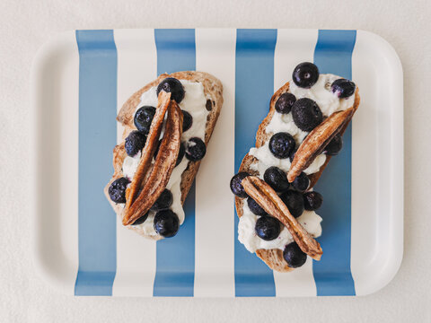 Creamy breakfast toast with blueberries, dried banana, served on a striped tray.