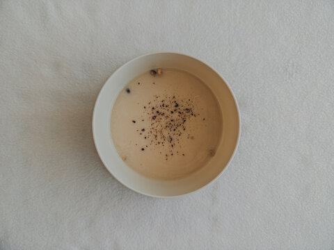 Creamy Soup with Black Pepper in a White Bowl on a Textured Background, Top View