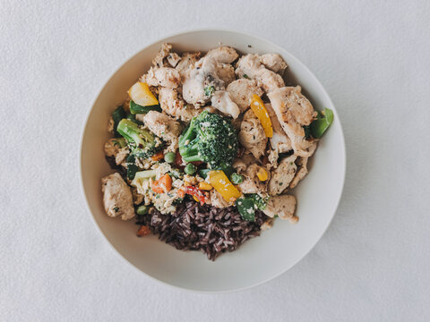 Healthy chicken and vegetable stir-fry with black rice served in a white bowl