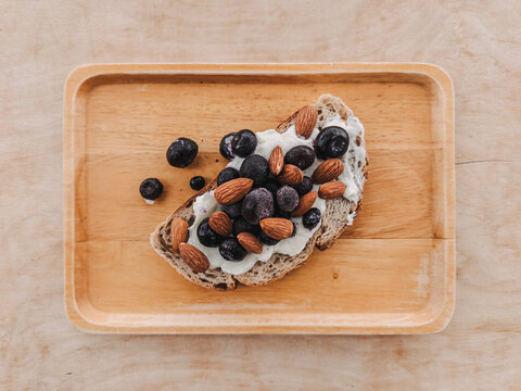 Healthy whole grain toast with cream cheese, blueberries, and almonds on a wooden tray.