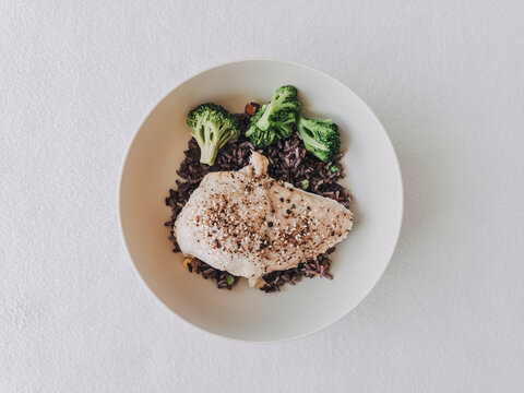Healthy Steamed Fish Fillet with Black Rice and Fresh Broccoli Florets on a White Plate