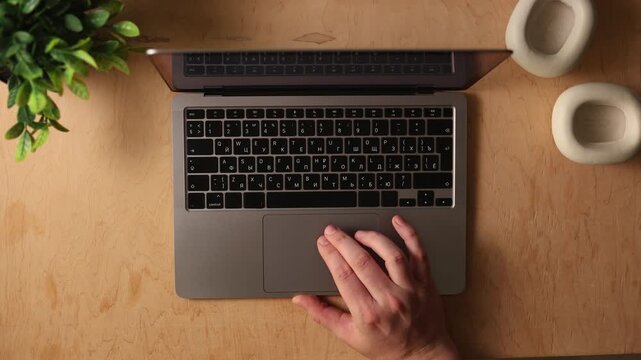 Overhead view of hands typing on a laptop with headphones and plant on desk