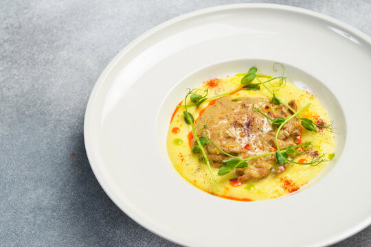 Savory stewed meat served over smooth potato puree in ceramic plate. Gourmet dish decorated with microgreens and chili oil. Delicious top view dinner table composition.