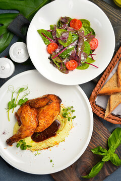 Tasty baked half chicken served over creamy mashed potatoes with gravy sauce. Fresh spinach salad with ripe cherry tomatoes sits near toasted bread. Delicious meal.