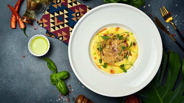 Savory stewed meat served over smooth potato puree in ceramic plate. Gourmet dish decorated with microgreens and chili oil. Delicious top view dinner table composition.
