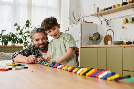 A father and his joyful son share laughter while stacking colorful dominoes together at home.