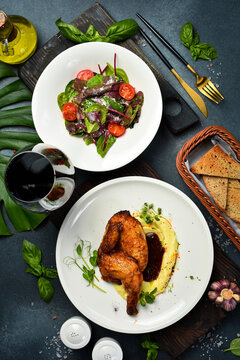 Roasted golden half chicken served over smooth mashed potatoes with savory sauce. Fresh vegetable salad with cherry tomatoes placed beside toasted bread basket. Delicious dinner.
