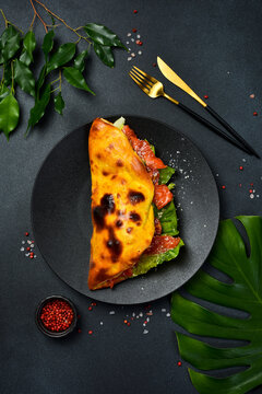 Tasty Italian folded pizza stuffed with smoked salmon. Fresh lettuce leaves and ripe tomatoes fill the baked dough. Delicious gourmet lunch served on dark dish.