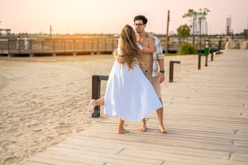 Obraz premium Playful pregnant couple dancing and embracing on a boardwalk by the beach at sunset.