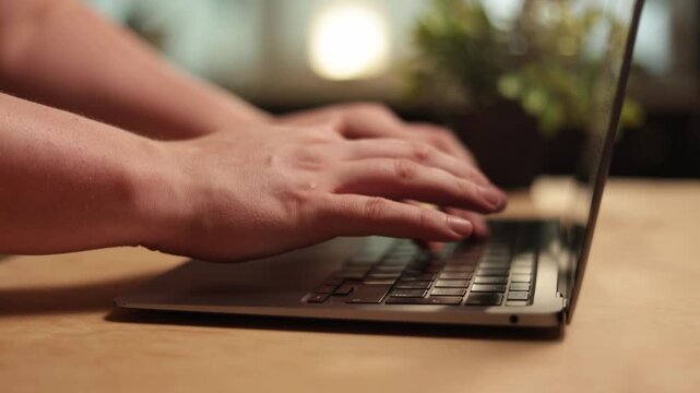 Close-up of hands typing on a laptop keyboard in a warm, ambient light setting