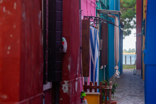 Colorful vibrant painted house walls and narrow alley passage leading to sea on Burano island near Venice Italy in summer sunlight