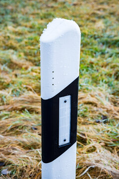 White and black delineator post covered with thin snow layer