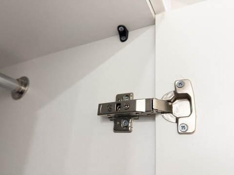 Close-Up View of a Metal Cabinet Hinge Installed on a White Cabinet Door, Showcasing Modern Design and Functionality for Seamless Operations