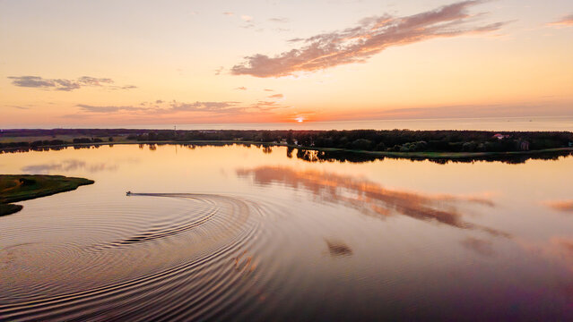 Aerial view of jet ski making circular wake on calm lake during golden sunset