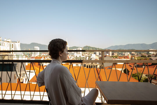cancer survivor sits quietly on a sunny apartment balcony overlooking the city, taking a restorative pause after treatment and reflecting on healing, freedom and new beginnings