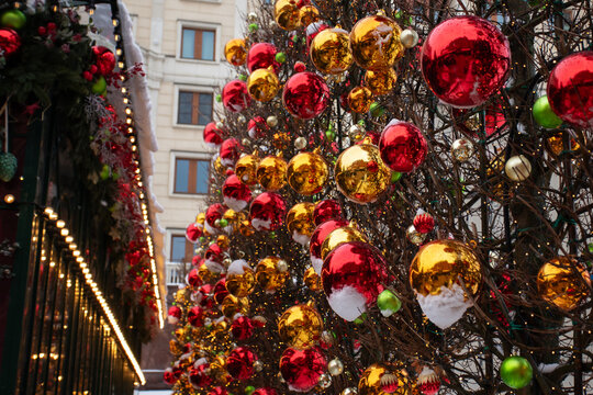 festive city street decorated with rows of bare trees covered in shiny red and gold christmas baubles, fairy lights and fresh snow, with historic building facades softly blurred in the background