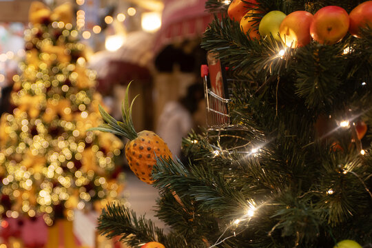 close view of a christmas tree decorated with citrus,apple and pineapple ornaments and warm fairy lights, creative seasonal decor idea, cozy festive atmosphere with soft bokeh