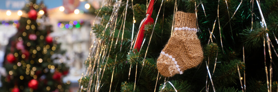 knitted sock decoration hanging on a green christmas tree with metallic tinsel and soft bokeh lights in the background, cozy handmade holiday atmosphere in a winter market