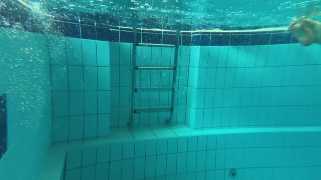 Adult woman practices an underwater forward somersault in an indoor swimming pool, improving body control, confidence, coordination, rotation, and swimming skills through training