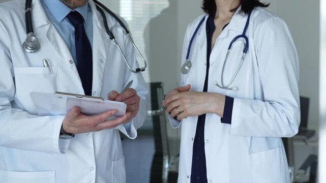 Medical experts in lab coats discussing patient information from a clipboard, representing collaboration, consultation, and professional healthcare dialogue in a clinic setting