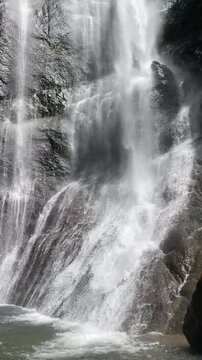 powerful mountain waterfall pours over dark wet rock walls, sending white spray and rushing water across layered stone in a dramatic close view of pristine forest wilderness