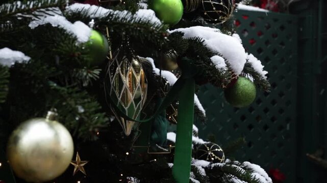 macro view of evergreen branch dusted with snow,decorated with green ribbon bow and shiny glass ornaments,soft holiday lights in background,cozy winter celebration concept