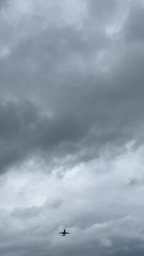 passenger airplane flies overhead beneath heavy gray storm clouds, creating a dramatic aviation travel scene with a dark moody sky and approaching weather