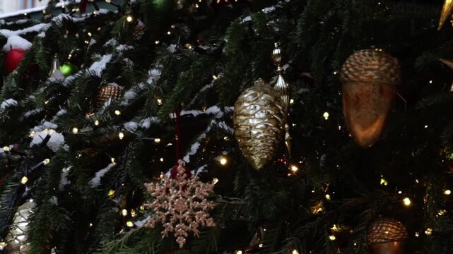 festive closeup of decorated fir tree with warm fairy lights,glittering gold pinecone and acorn ornaments,light snowfall on branches,moody winter holiday background