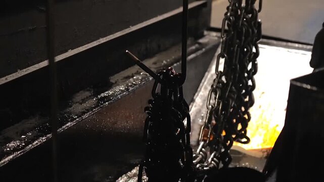 Industrial machinery processes heavy metal chains through automated quenching lines and heat treatment baths inside a manufacturing facility plant workshop