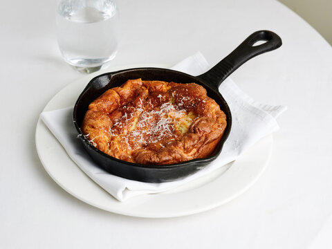 Dutch baby pancake with melted cheese in a cast iron skillet for brunch and cafe menu ideas