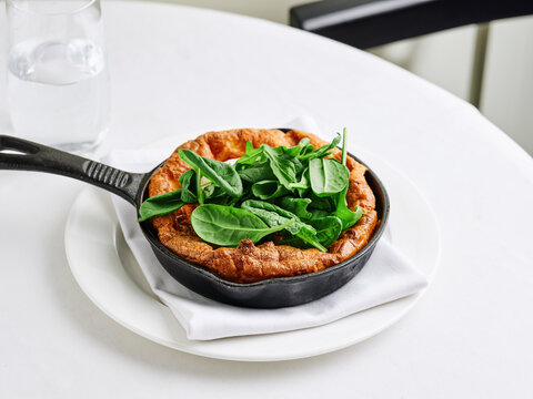 Dutch baby pancake with avocado and baby spinach leaves, served in a cast iron skillet, brunch menu, healthy eating concept