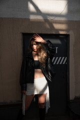 Fototapeta premium Stylish young woman in a leather jacket posing outdoors in urban sunlight