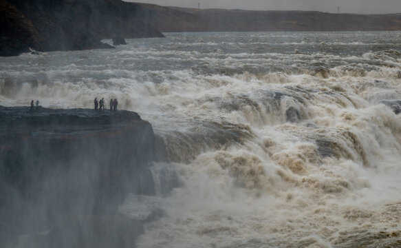 TTourists standing on a cliff at gullfoss, experiencing the immense power of the golden waterfall and glacial river hvita. Iceland golden circle tourism route