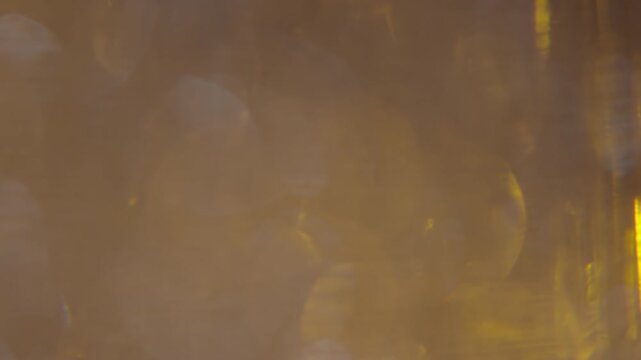 The video background features sparkling golden shimmering objects floating in a liquid, conveying a sense of luxury and sophistication.