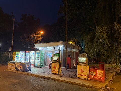 Belgrade, Serbia - June 22, 2026: Night view of small retro independent Art Petrol gas station with vintage fuel pumps. Retro design. Not covered. Illuminated beverage vending machines.