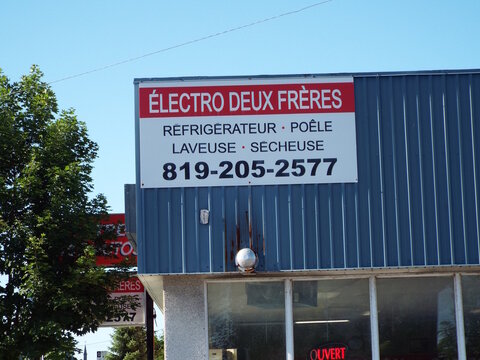 Gatineau, Quebec, Canada &ndash; June 19, 2026: A sign for "&Eacute;lectro Deux Fr&egrave;res" detailing appliances and a phone number is mounted on a blue corrugated building facade on Bd Gr&eacute;ber.