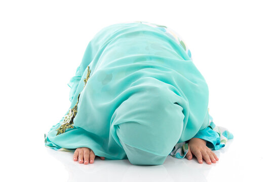Charming young Asian Muslim child in traditional headscarf bowing down in prayer during holy month Ramadan.