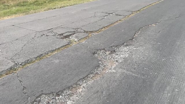 Damaged asphalt road with deep cracks and potholes