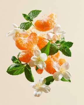 Burst of tangerine segments and white jasmine flowers with fresh green mint leaves against a soft beige background, showcasing vibrant colors and natural elements