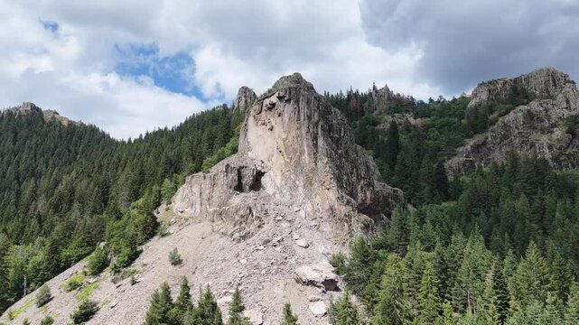 Aerial fly-in shot of a massive rocky cliff and scree slope surrounded by pine forest