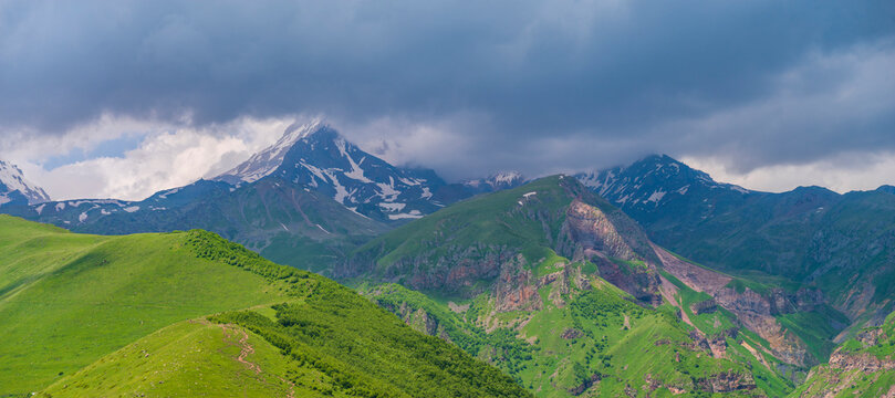 Mount Kazbek in clouds behind green hills of Caucasus, panoramic Georgia landscape with copy space