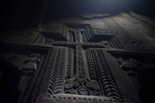 Ancient Armenian carved cross khachkar in dark Geghard monastery, wide panorama with copy space